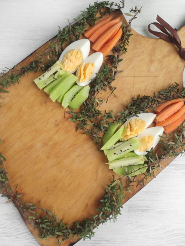 A wooden board with arranged boiled eggs, carrots, and kiwi slices