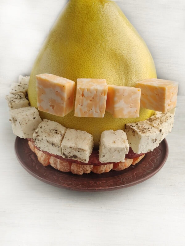 Pomelo surrounded by diced young cheese with herbs and cubes of marbled cheese on top of tangerine slices