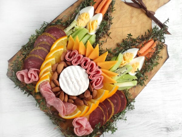 A charcuterie board with cheese, almonds, orange slices, meats, and boiled eggs arranged in a decorative pattern.