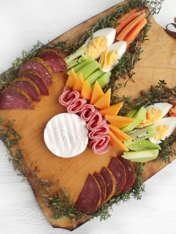 A charcuterie board featuring eggs, vegetables, cheese, and salami, arranged beautifully.