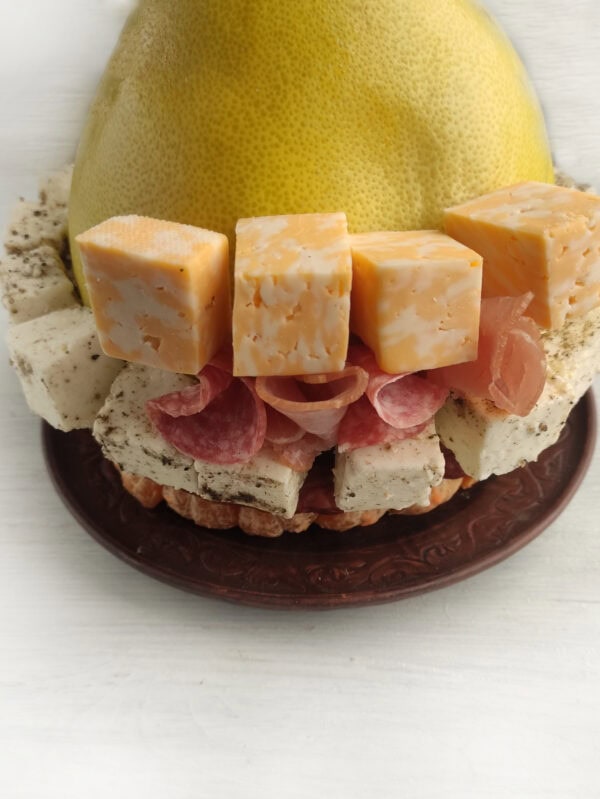 Pomelo surrounded by diced young cheese with herbs and cubes of marbled cheese on top of tangerine slices with added salami slices folded in quarters