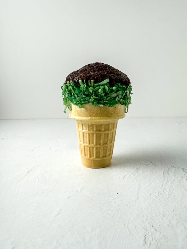 Chocolate cupcake inserted into the top of the ice cream cone with green shredded coconut around the ri