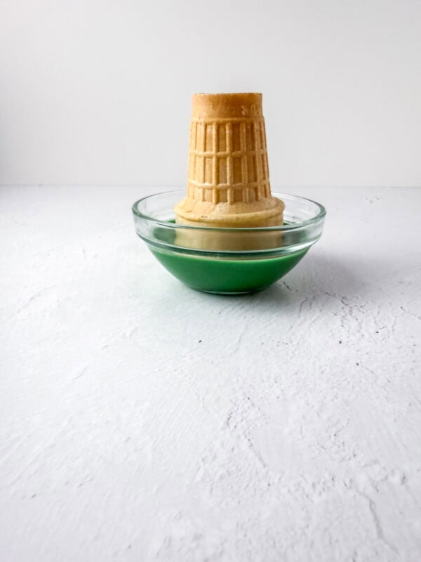 Ice cream cone dipped upside down in a bowl of melted green candy coating