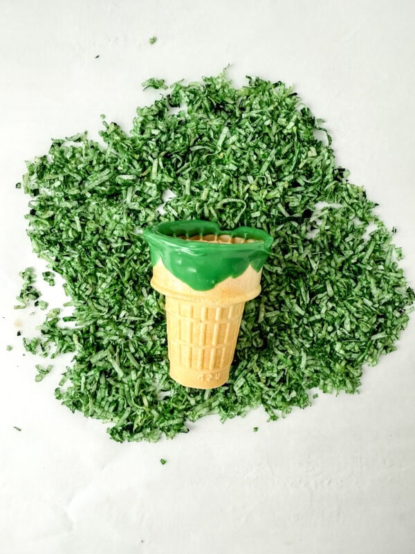 Ice cream cone coated with green candy and covered in green shredded coconut