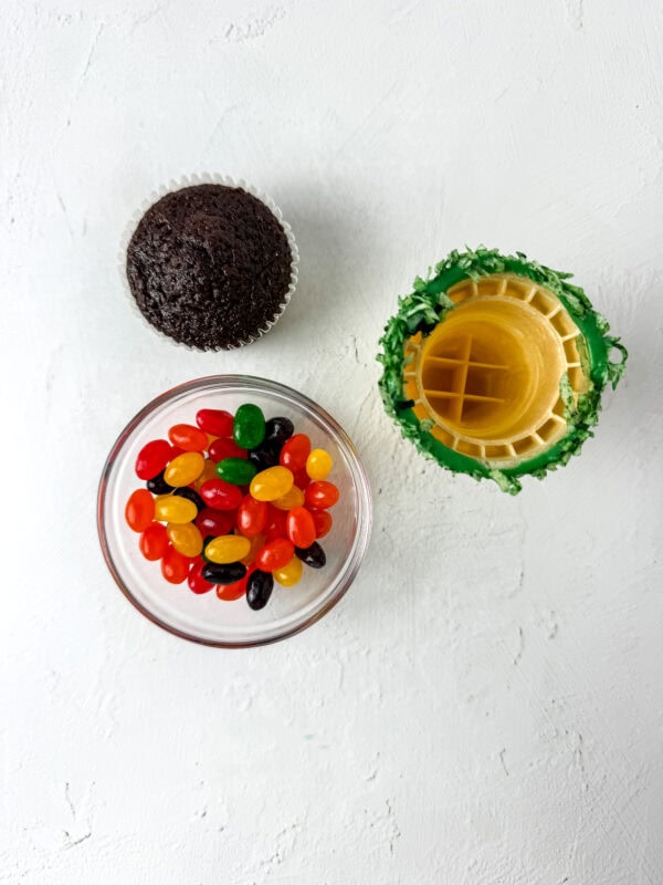 Chocolate cupcake, jelly beans in a bowl, and an ice cream cone with shredded coconut around the top