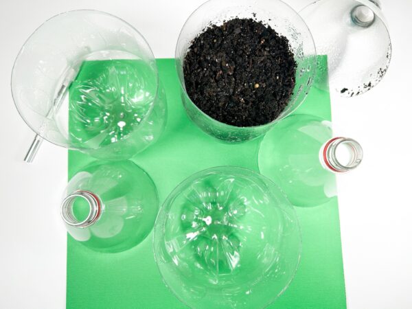 Top-down view of bottle pieces and soil-filled containers on the green surface