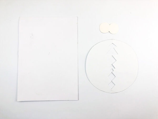 White paper pieces cut into shapes for a chick and an eggshell.