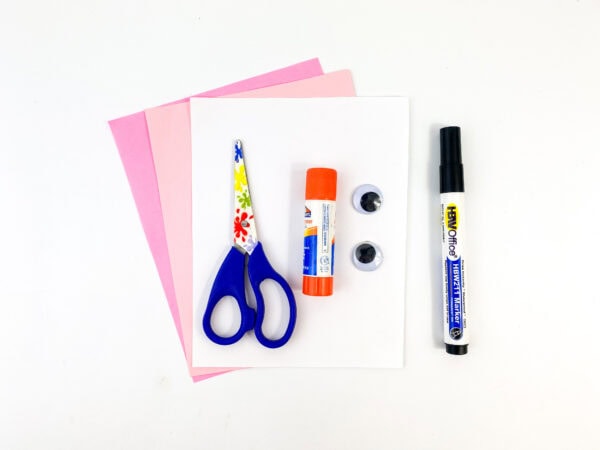 Craft supplies including scissors, glue stick, googly eyes, a black marker, and pink and white paper.