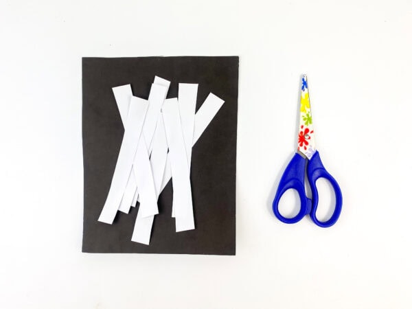 White paper strips and a pair of scissors on a black paper.