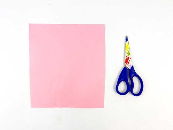 A square piece of pink paper with scissors beside it.