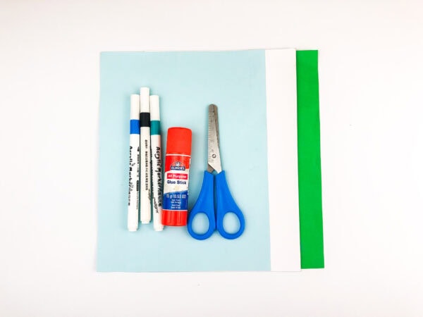 Craft supplies including blue, white, and green paper, glue stick, scissors, and markers.