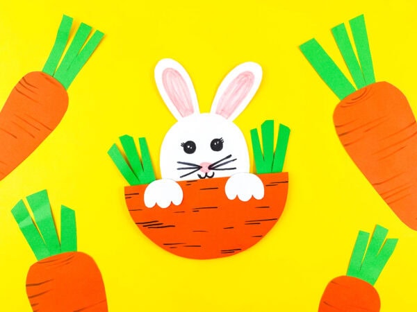 A paper bunny in a carrot pocket, surrounded by paper carrots on a yellow background.