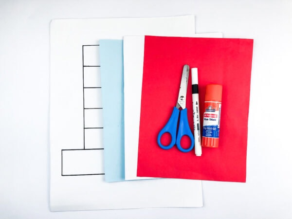 A set of craft supplies including white, blue, and red construction paper, a pair of scissors, a black marker, and a glue stick