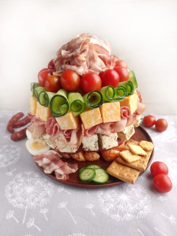 Charcuterie tower arranged in layers, featuring a variety of meats, cheese cubes, cherry tomatoes, and cucumber spirals