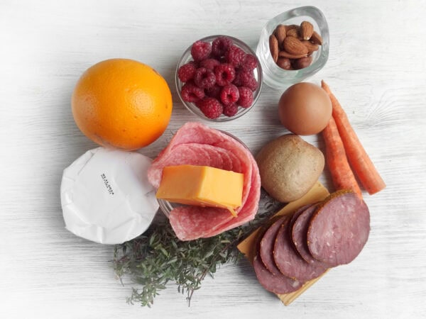 Ingredients for the charcuterie board, including an orange, cheese, nuts, raspberries, salami, and a boiled egg