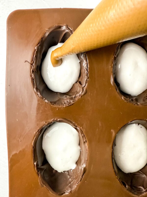 Piping cookie butter onto marshmallow-filled chocolate egg molds.