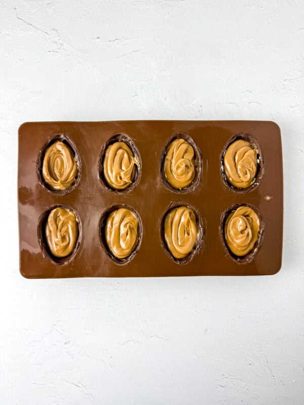 Chocolate egg molds filled with cookie butter on top of a marshmallow layer.