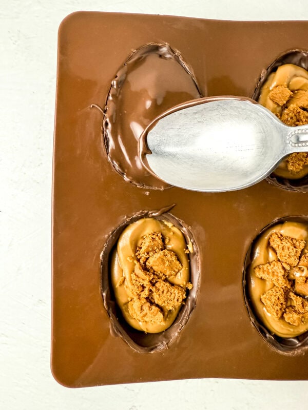 Sealing the cookie butter-filled chocolate eggs by spreading melted chocolate over the mold.