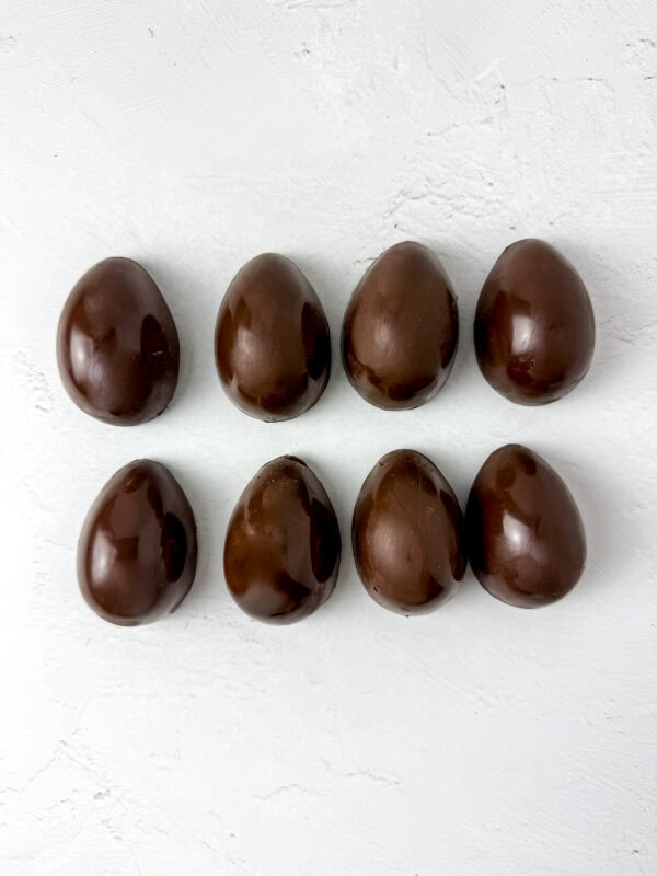 Eight glossy chocolate egg-shaped shells arranged on a white surface.