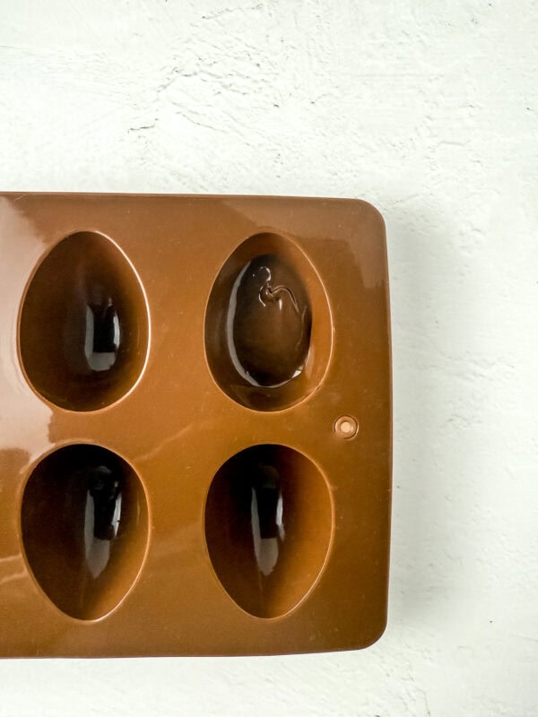 Silicone egg mold with melted chocolate partially spread inside one cavity.