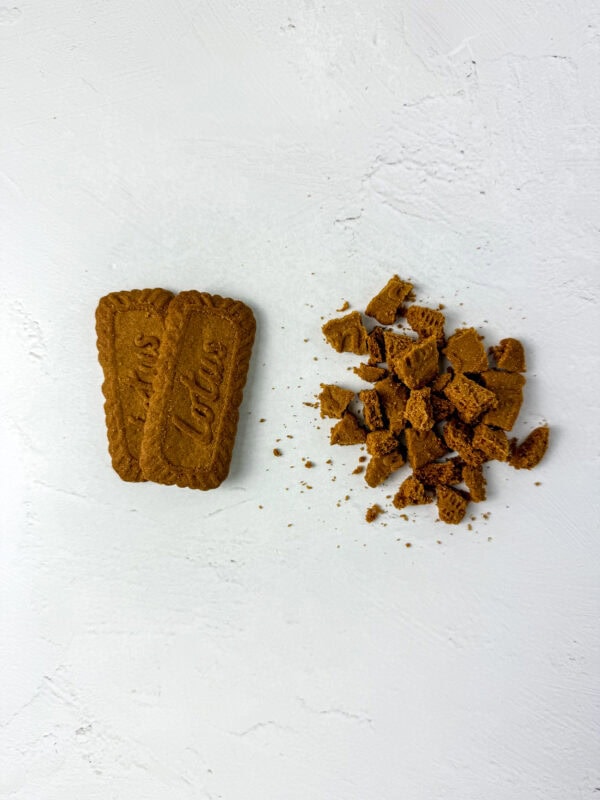 Two whole Biscoff cookies on the left and crushed Biscoff cookies on the right, scattered on a white surface.