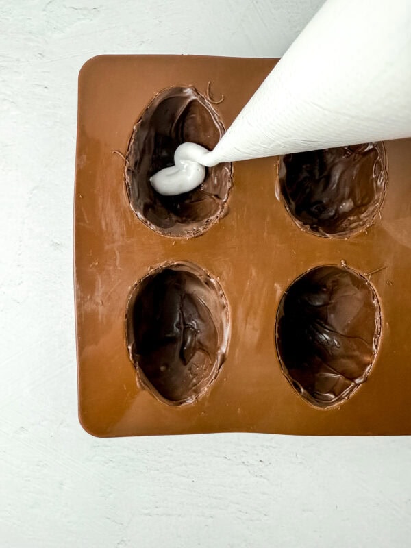 Piping marshmallow fluff into a chocolate-coated egg mold.