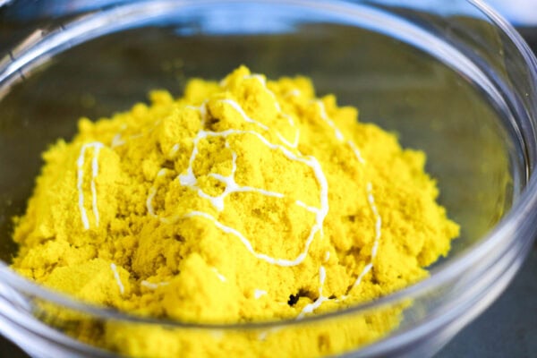 A close-up of yellow kinetic sand in a bowl, with glue over it.