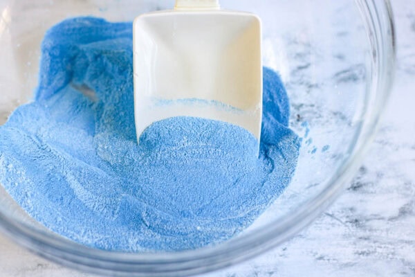 A bowl filled with dry blue colored sand being stirred with a white scoop.
