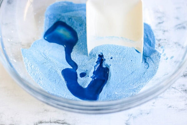 Liquid dish soap being poured onto the blue sand mixture in the bowl.