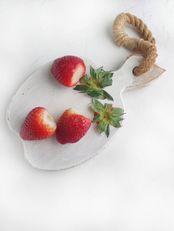 Strawberries with tops removed placed on a white cutting board.