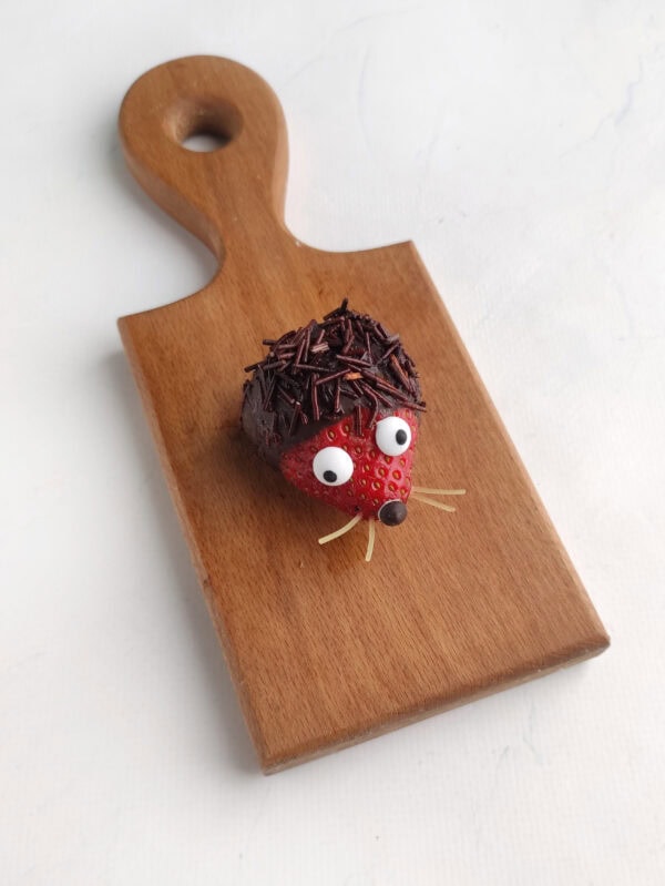 Close-up of a single strawberry hedgehog on a small wooden board.