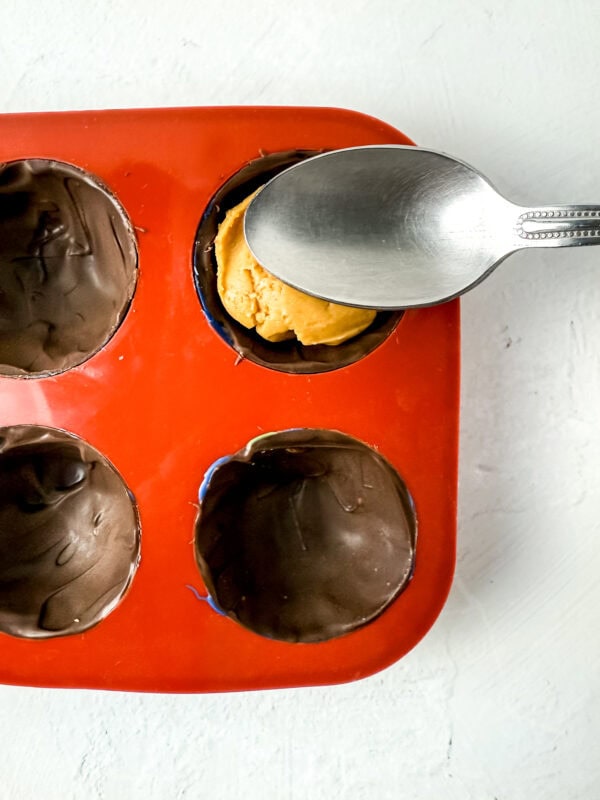 Spoon pressing peanut butter filling into the chocolate-lined mold.