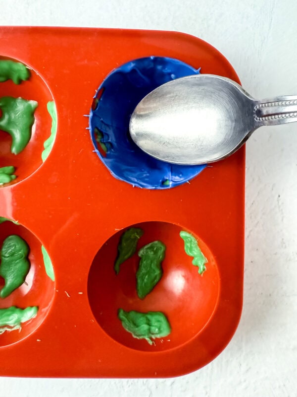 Blue candy melt being spread inside the mold using a spoon.