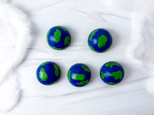 Five finished Earth-shaped chocolate domes on a marble surface.