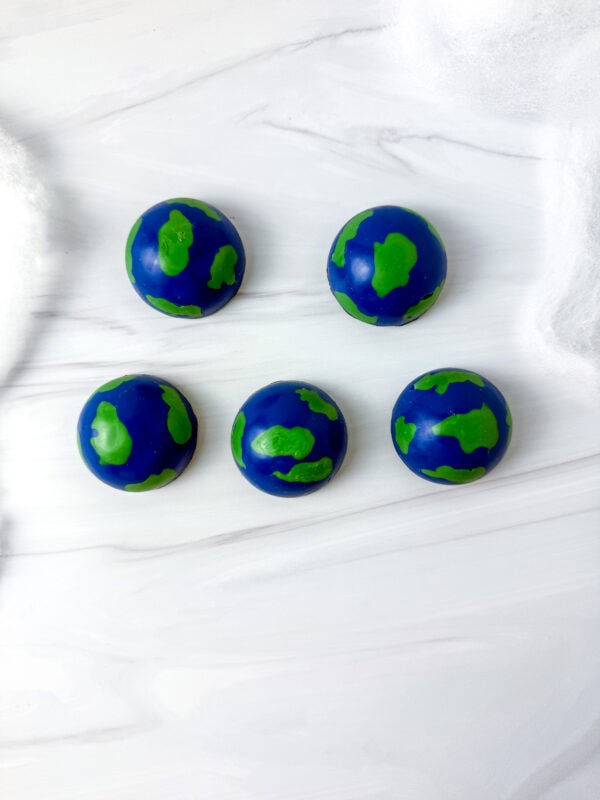 Top view of five Earth-shaped chocolates on a marble surface with cotton decoration.