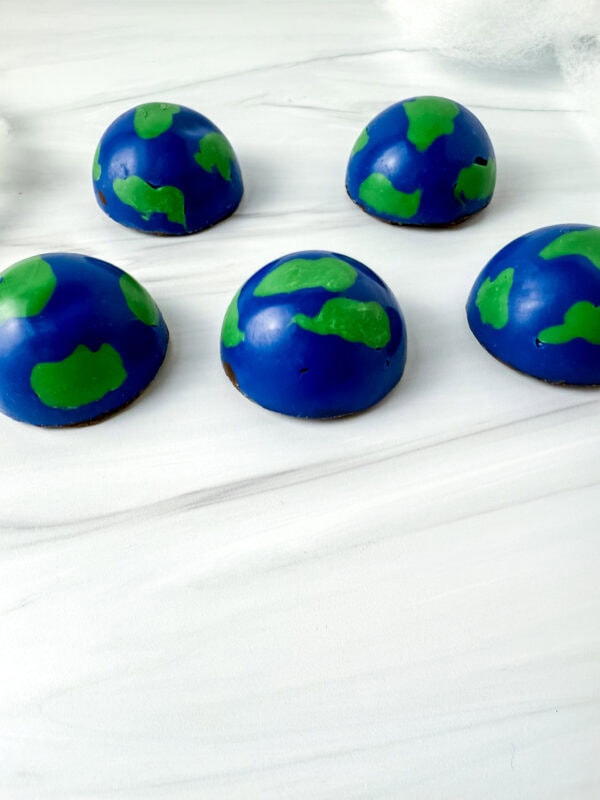 Side view of Earth-themed chocolate domes arranged on a white surface.