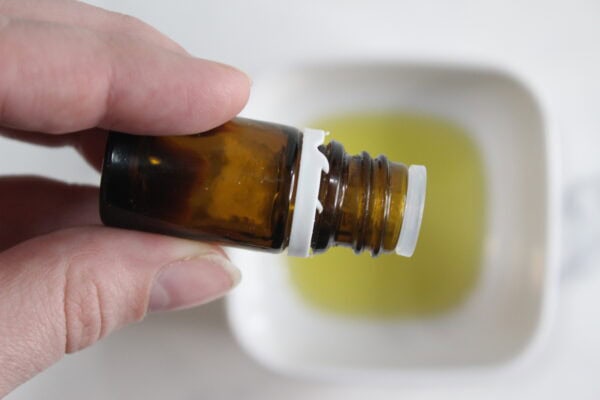 Essential oil bottle held over a bowl of oil.
