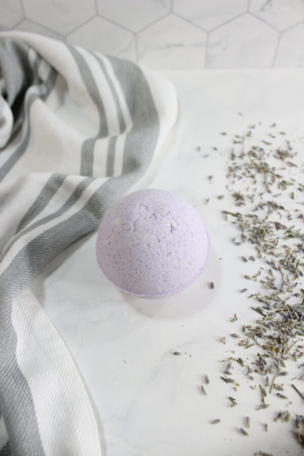 Half view of lavender bath bomb near towel and herbs.