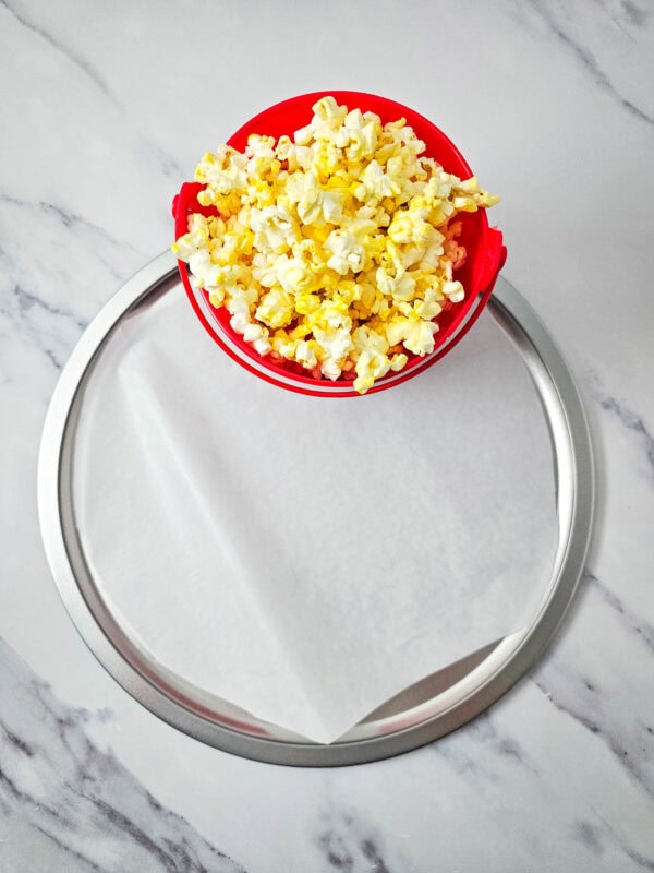 A red popcorn bucket placed on a parchment-lined round tray, ready for snack arrangement.