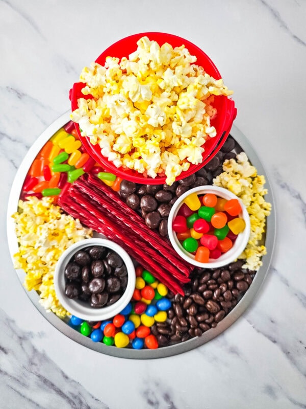 A completed candy charcuterie board topped with a bucket of popcorn and surrounded by candy and chocolate sections.