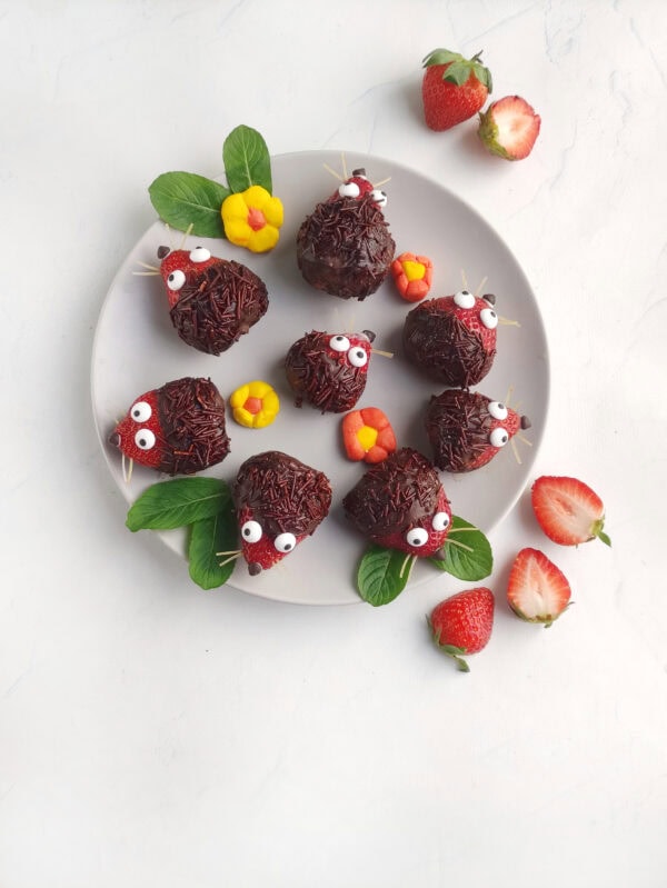 Overhead view of strawberry hedgehogs arranged on a plate with flowers and mint.