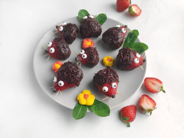 Side angle of the plate filled with strawberry hedgehogs and strawberry halves.