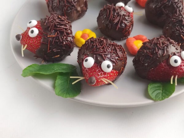 Close-up of a strawberry hedgehog with candy eyes, sprinkle “spikes,” and mint garnish.