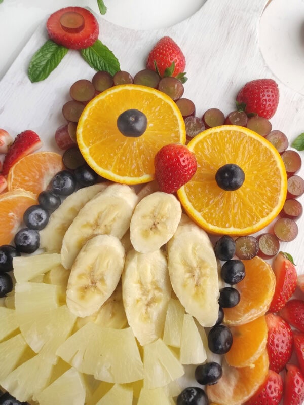 Front-facing view of a fruit owl on a white board surrounded by strawberries and mint leaves.