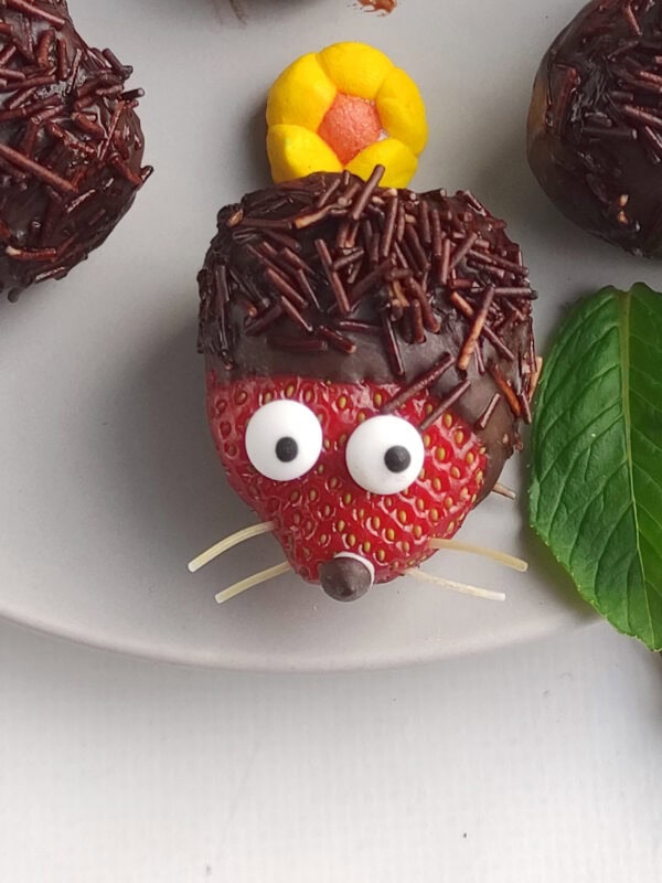 Detailed view of a strawberry hedgehog’s face with candy eyes and whiskers on a plate.
