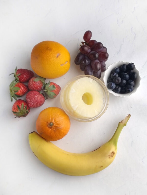 Assorted fruits including banana, orange, tangerine, strawberries, grapes, blueberries, and a jar of pineapple slices.