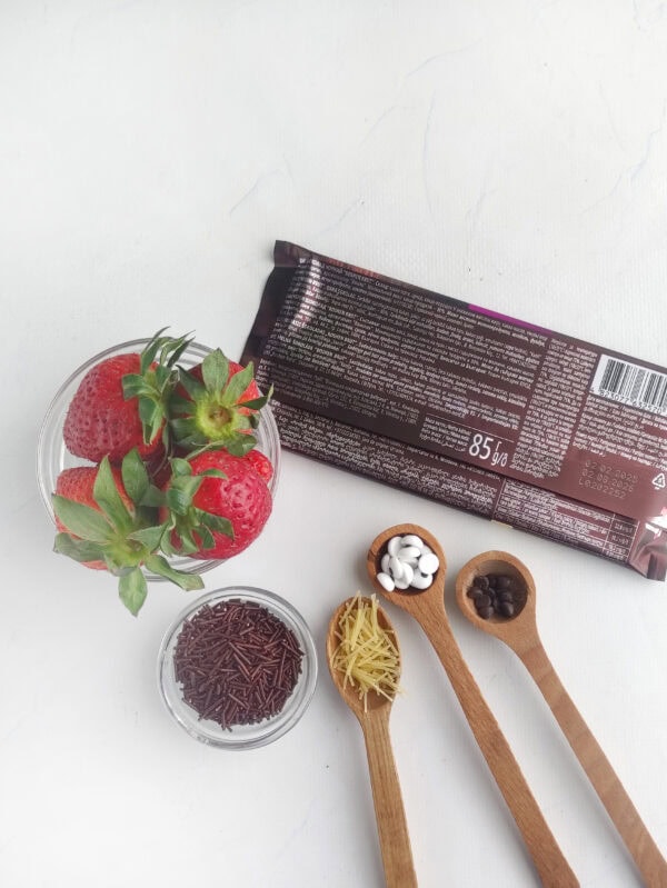 Ingredients including strawberries, dark chocolate, candy eyes, sprinkles, and pasta whiskers.