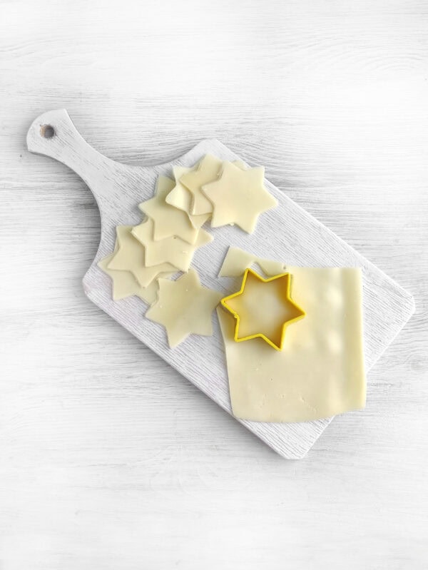 Cheese slices being cut into star shapes using a yellow star-shaped cookie cutter on a white cutting board.