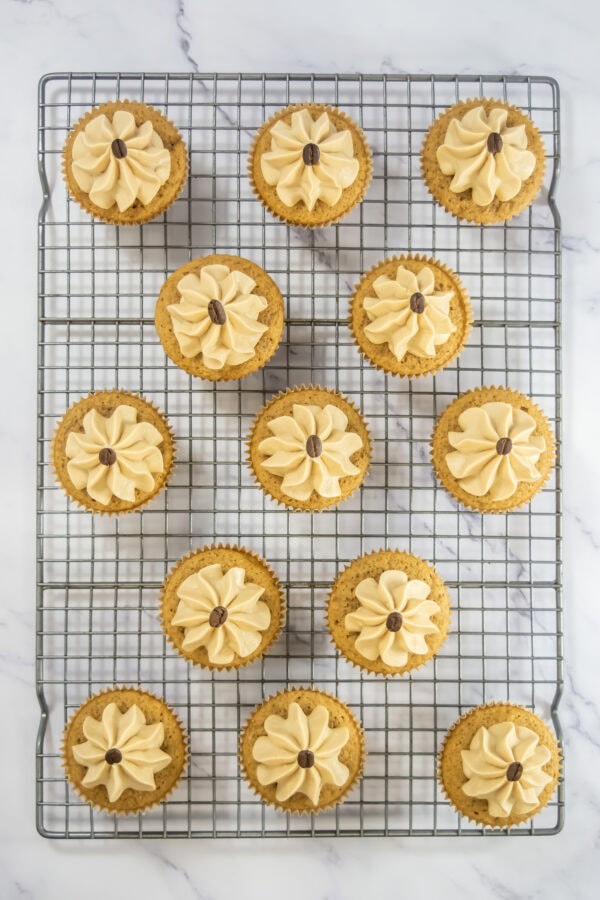 Frosted espresso cupcakes with coffee beans on a wire rack.