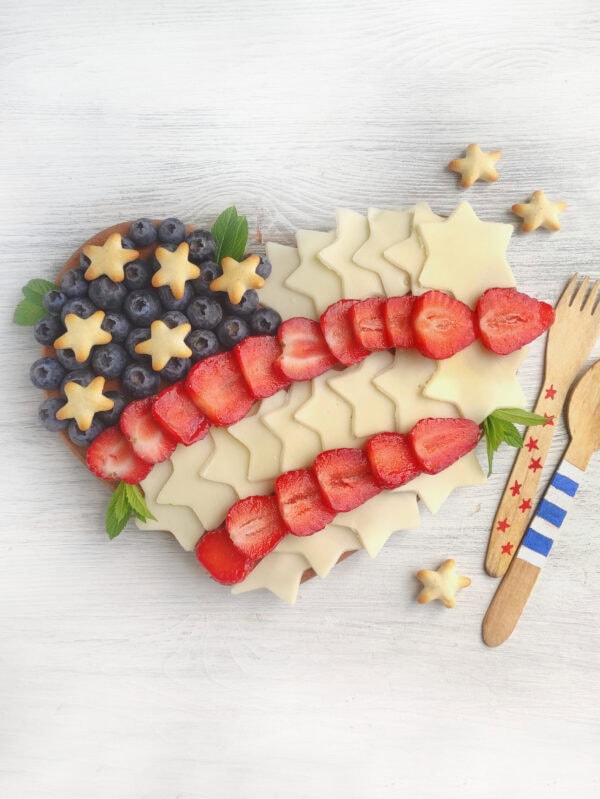 Finished patriotic charcuterie board on a wooden surface featuring cheese stars, strawberries, and blueberries arranged in a flag shape.